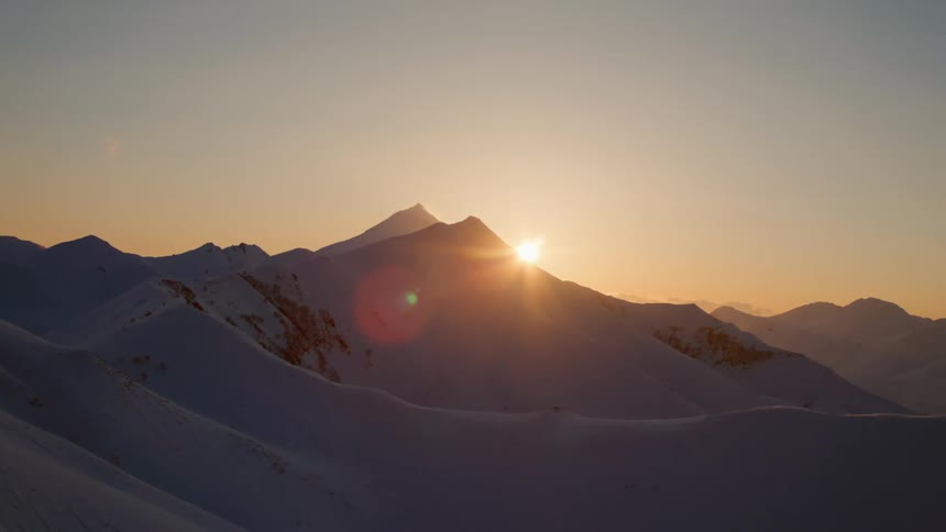 The sun rises from behind a snowy mountain