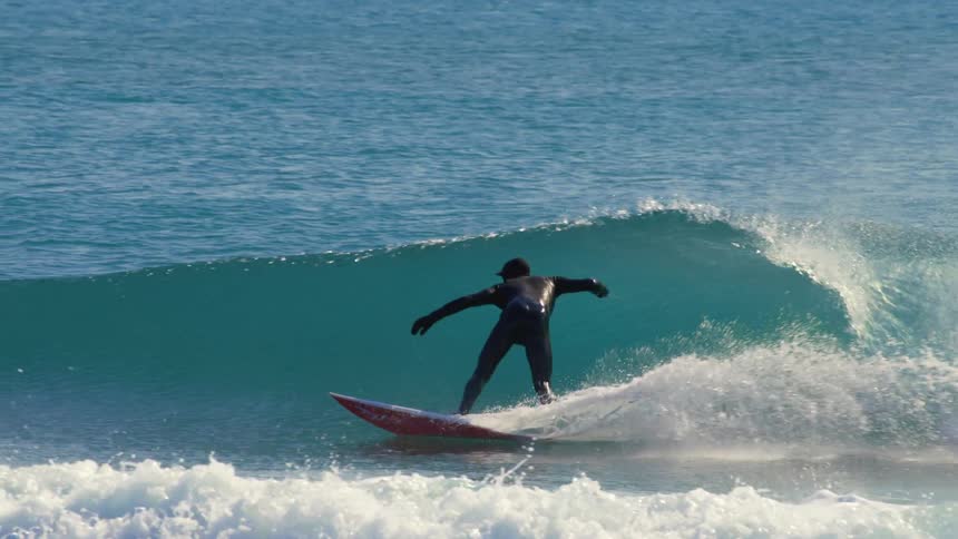Water splashes as a surfer wearing a wetsuit rides a wave into shore