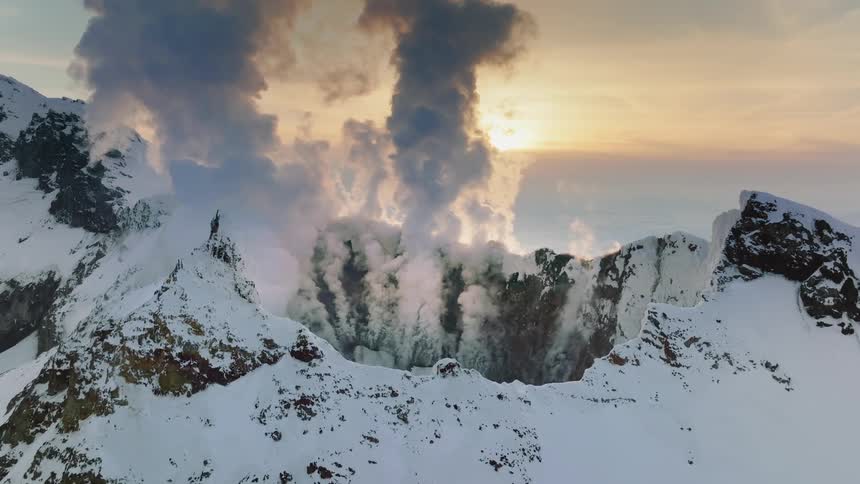 A dramatic volcanic eruption illuminates the snowy mountaintop casting a fiery glow against the twilight sky
