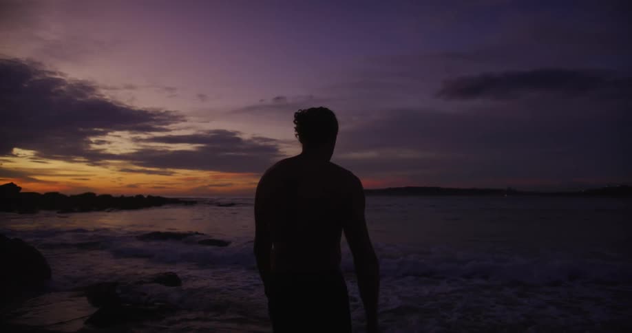 A man is walking into the ocean at sunset