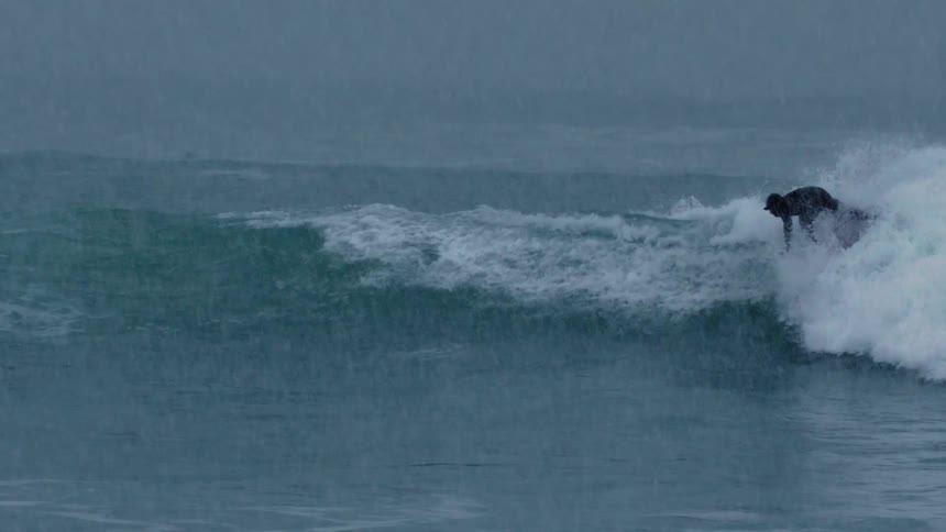 Man is surfing on waves while its raining heavily outside