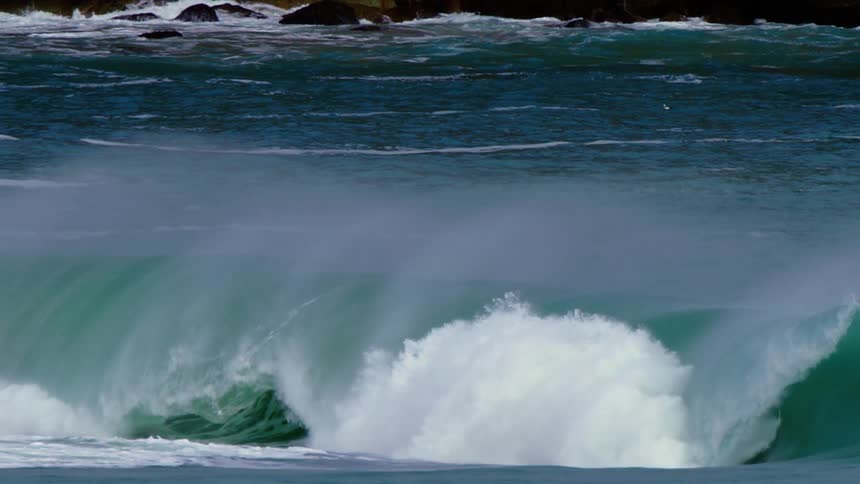 A powerful wave crashing against a shore with foamy white water against a deep blue ocean