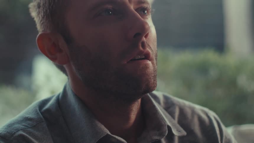 A man sitting on a couch reads something looks confused and shakes his head