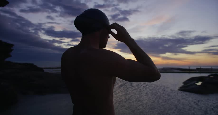 Swimmer with cap adjusts his equipment while looking at the horizon in front of the sea