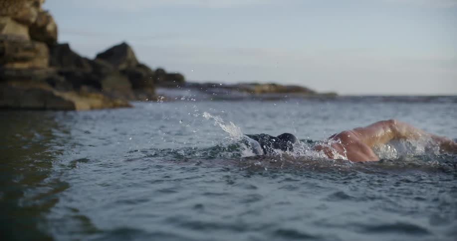 A man is swimming in the ocean near a rocky coastline