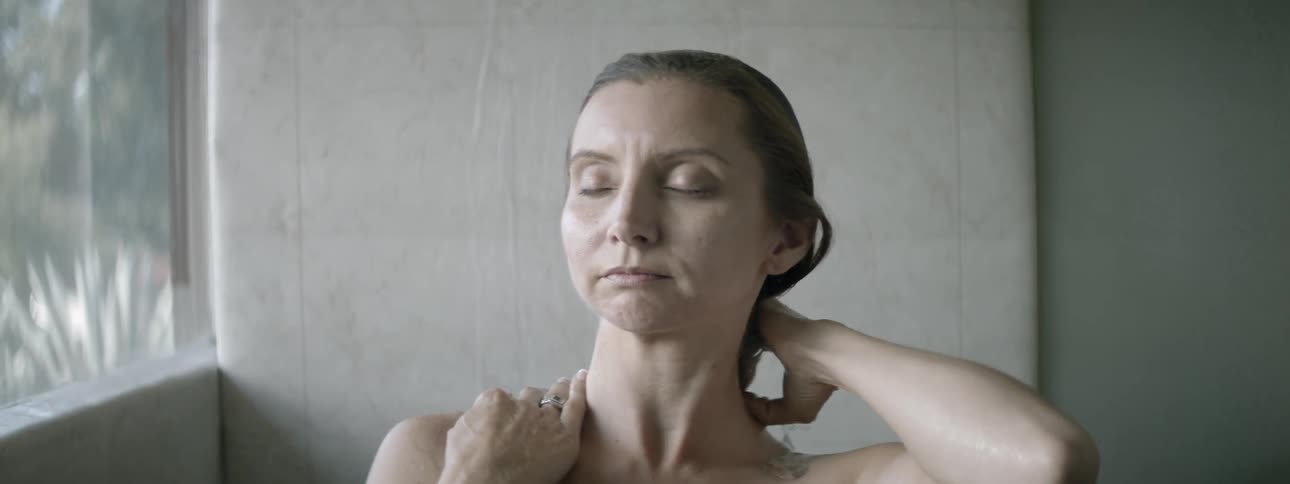 A woman standing in a shower and wetting her hair down