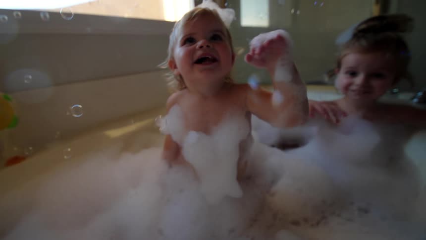 Two girls play with soap bubbles while taking a bath in a bathtub