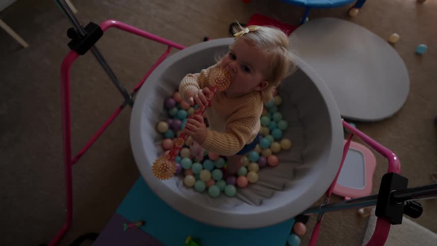 A girl standing on a small ball pit in a play room chewing on a wand