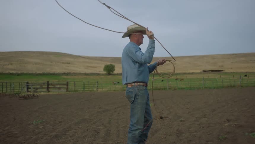 A cowboy is swinging a lasso above his head