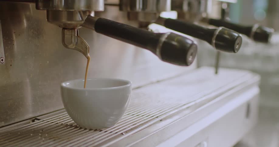 Machine coffee being poured into a small ceramic cup