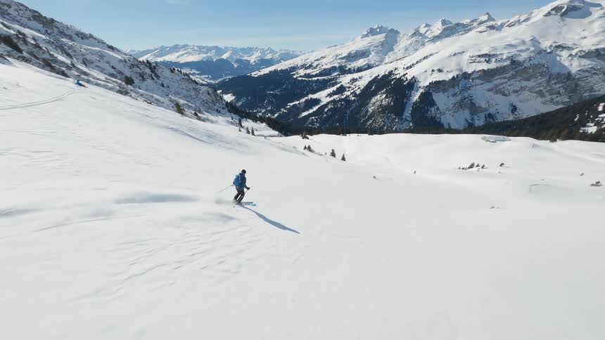 A skier is descending a snowy mountain slope with a backdrop of snowcovered peaks and a clear blue sky in switzerland