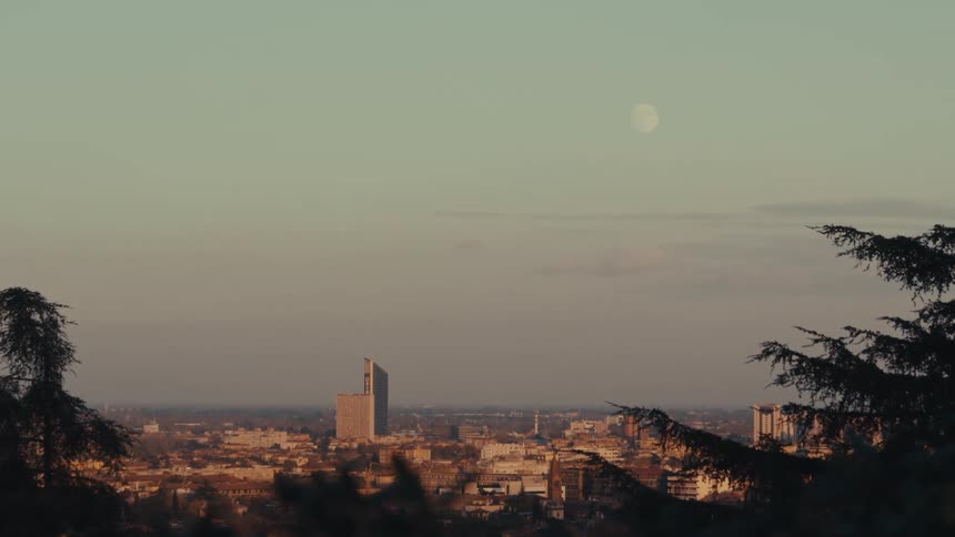 A view of a city with a huge building in the middle on a clear day with a moon in the sky