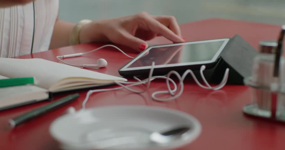 Close up of a table with a tablet and a hand reaching for a cup of coffee