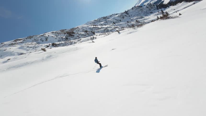 Drone view of a person skiing down the snowy slope of a mountain on a sunny day in Switzerland