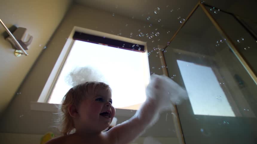 A baby playing with soap bubbles while taking a bath