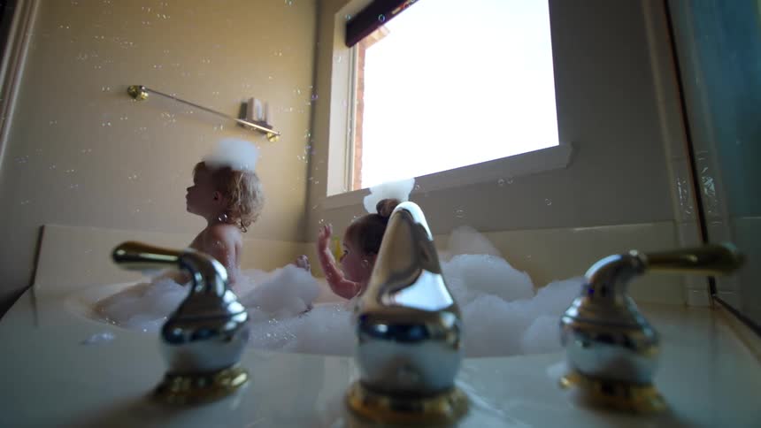 Two twin girls playing in a bathtub with foam in soap bubbles