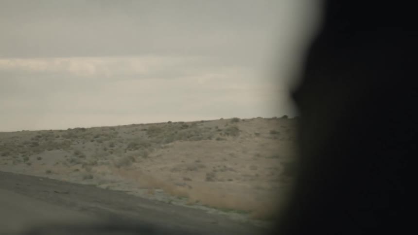 A man sleeping in a car being driven through a desert