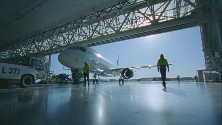 Two workers walking along a tow tractor pulling an airplane inside a hangar