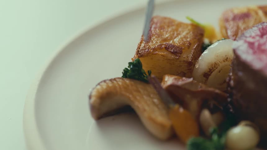 Metal tongs placing a vegetable in the middle of meat on a plate