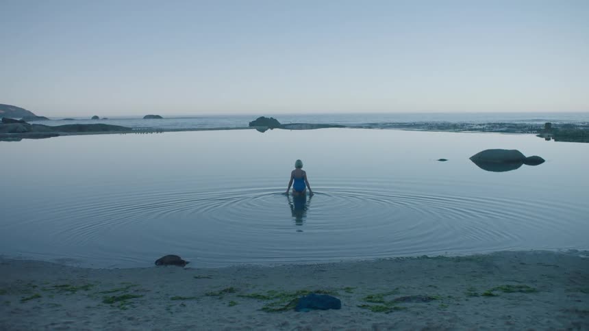 Woman in blue swimsuit entering a lake by the sea