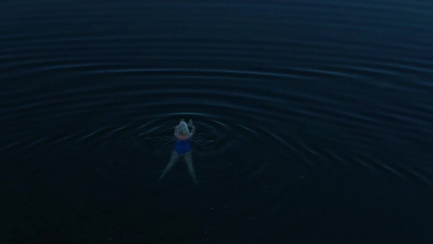 White haired woman swims in a pool near a shore frequented by many floating animals