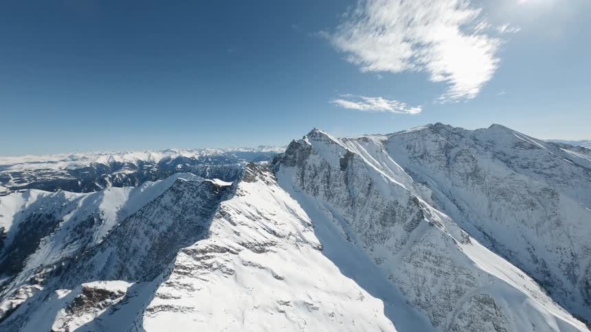 Aerial view of a jagged ridge of snowcapped mountains stretches across a vast almost cloudless sky in Switzerland