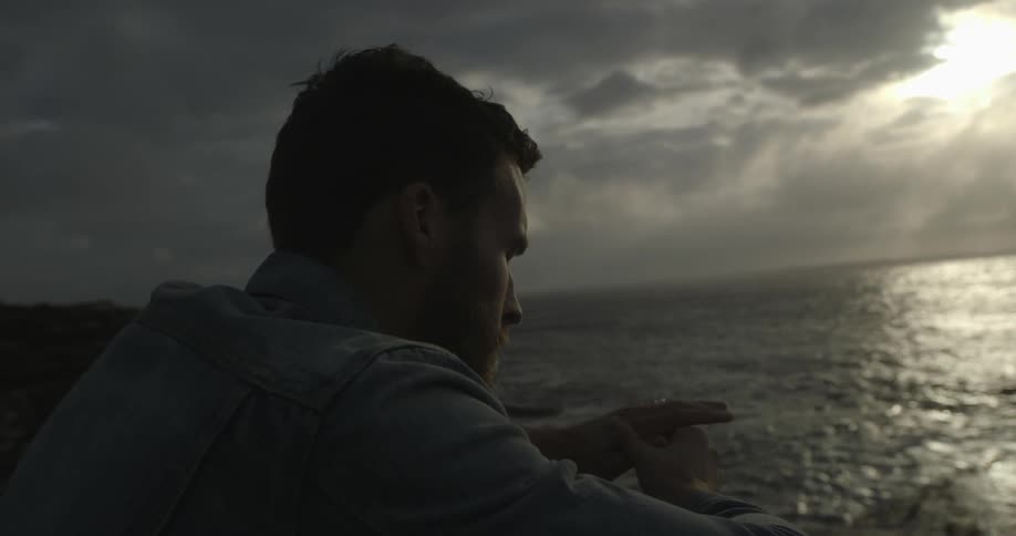 Man sits by the water at sunset