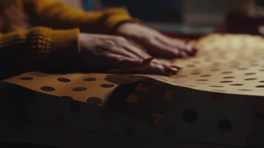 A woman is wrapping a gift and pressing down the wrapping paper