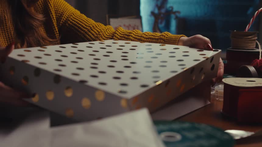 Womans hands closing a gift box on the table