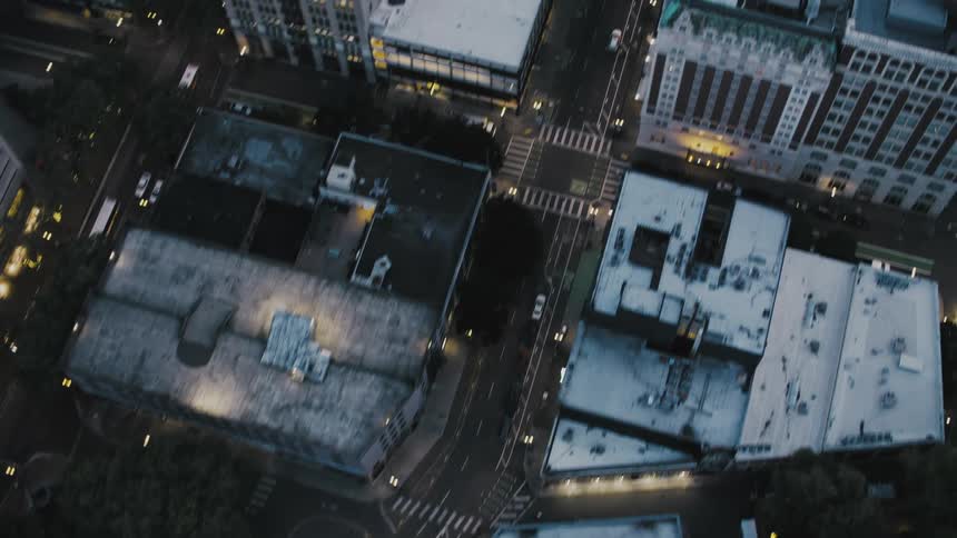 An aerial view of a city at night shows a busy intersection with cars driving along the roads and lights illuminating the buildings