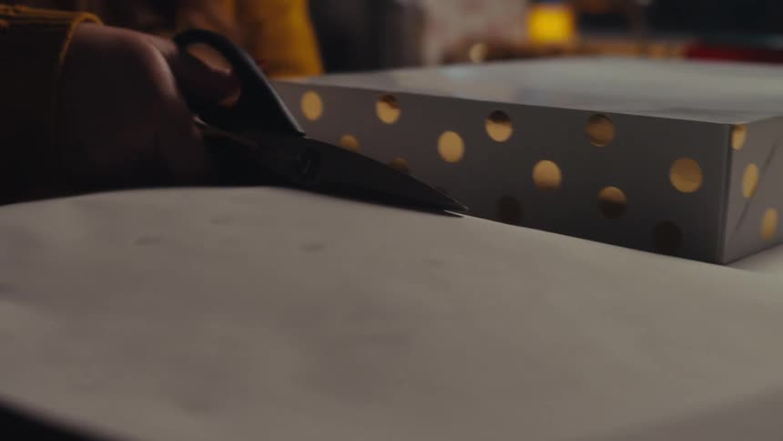 A persons hand using scissors to cut a piece of white cardboard