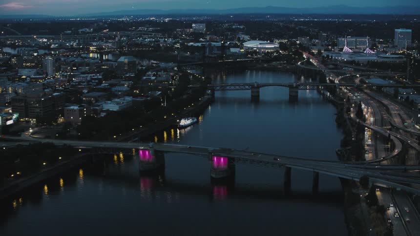 An aerial view of a city at dusk with a river flowing through it and several bridges lit up with pink lights