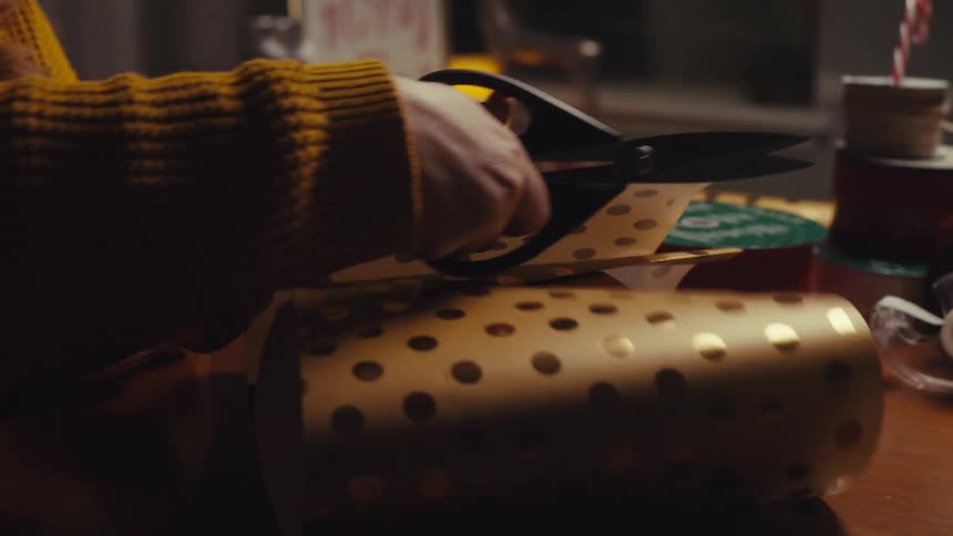 A persons hand using scissors to cut wrapping paper for a red box
