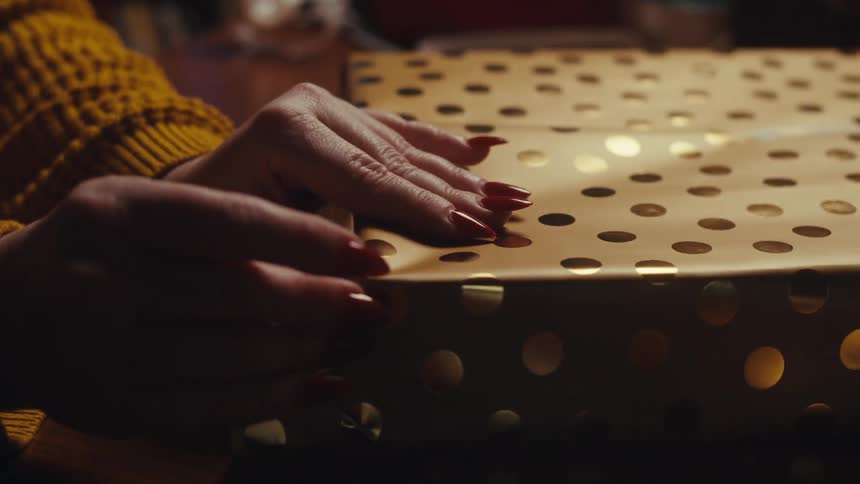 Closeup of hands wrapping a present in bright gold paper