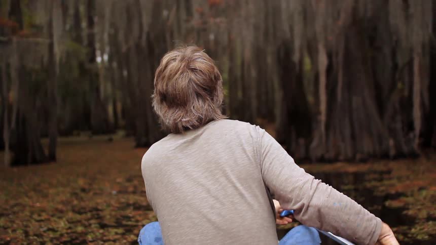 A man kayaks down a river lined with trees