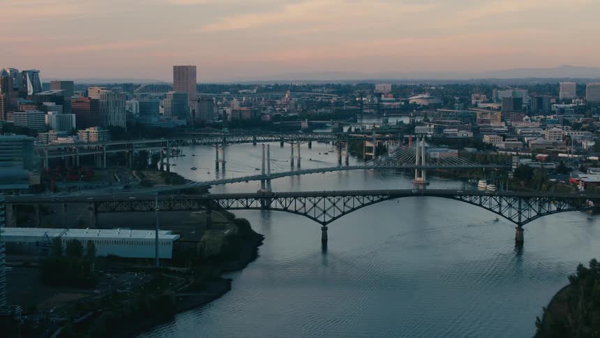 Several bridges span the willamette river as it flows through portlands cityscape under a dusky sky