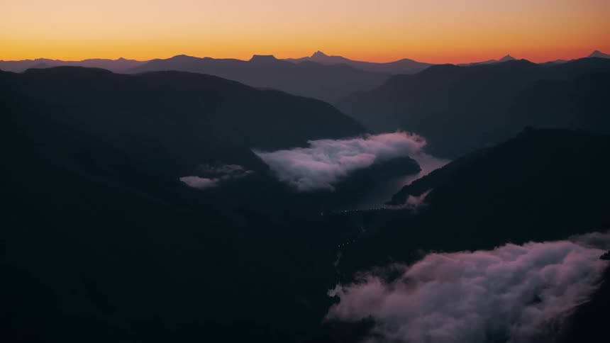 Silhouetted mountains rise against a fiery sunset sky with a river winding through a valley below