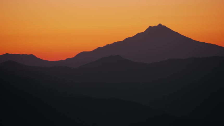 Silhouettes of mountains across the landscape under an orange sunset sky