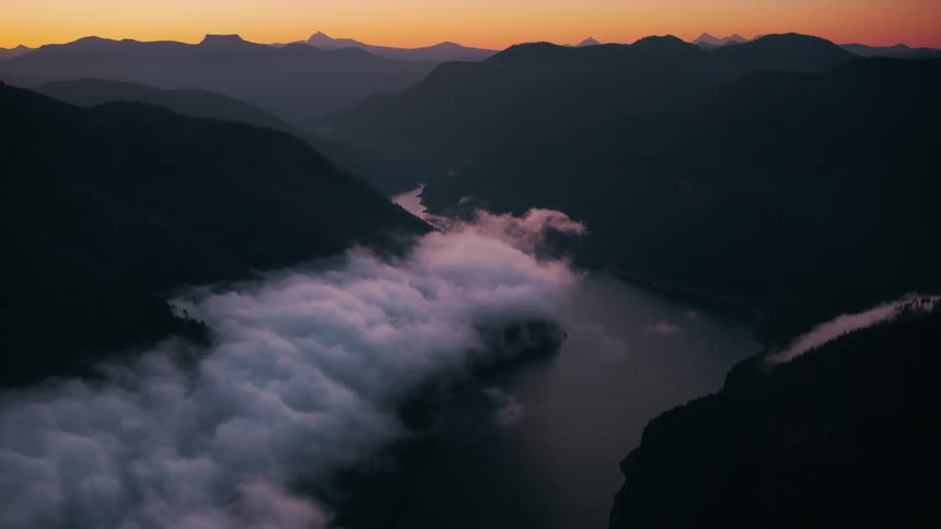 Silhouetted mountains rise against a fiery sunset sky with a river winding through a valley below