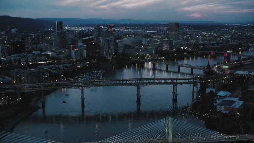 The cityscape dominated by a river reflecting its lights is crisscrossed by illuminated bridges forming a glowing network while a mosaic of lights from buildings and streets illuminates the night sky