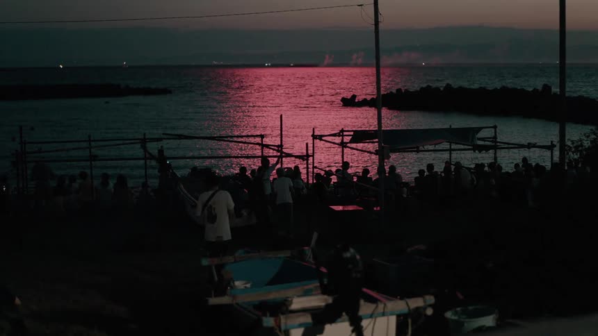 A crowd watch a firework show by the shore