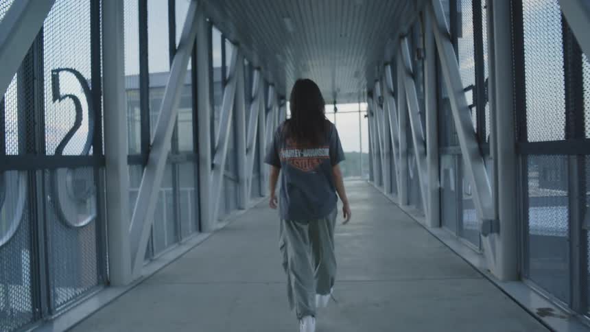 Young woman walks alone along a covered walkway with a metal structure and glass walls