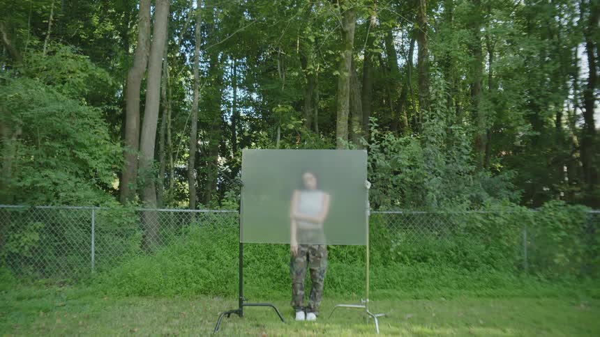 A woman stands behind a screen that obscures her face