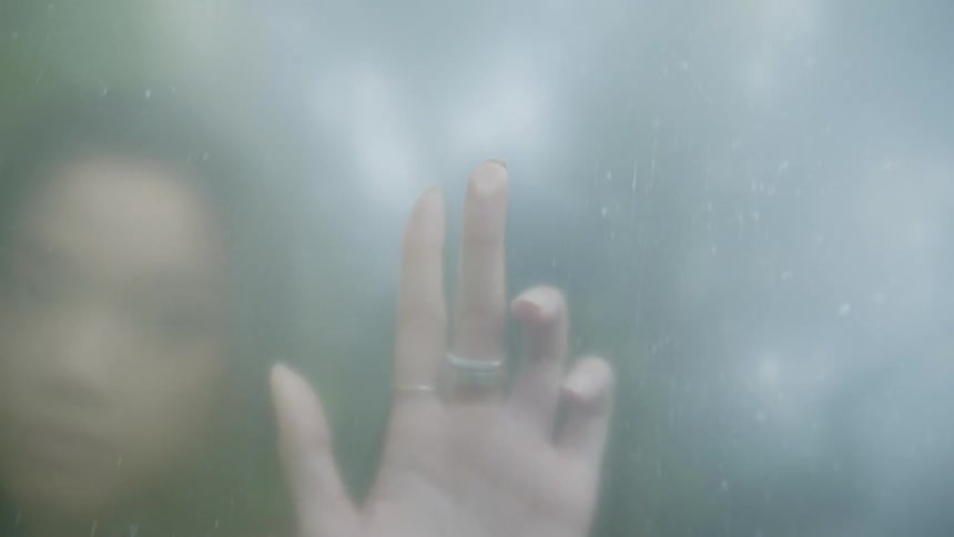Woman is seen through a blurred surface her hand outstretched and touching the glass