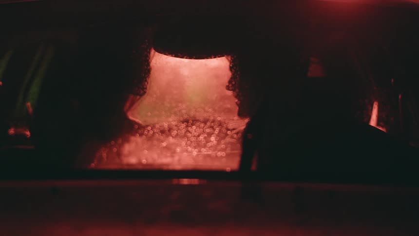 Silhouette of two people inside a car seen through the fogged windshield and illuminated by a soft reddish light