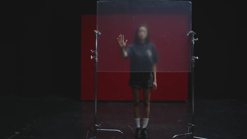 Woman in a studio behind a glass plate putting her hands together