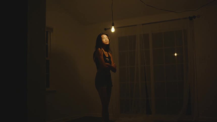 Woman with her arms crossed while standing in an empty room with a light on in front of her