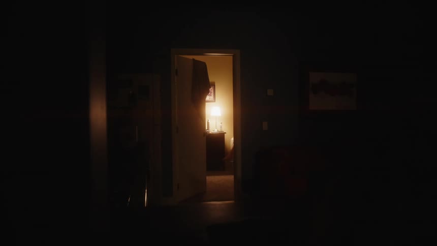 Barefoot woman climbs onto a bed in a bedroom lit by a lamp at night