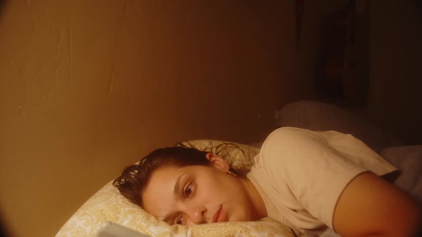 A woman lying in bed in her bedroom turns off the light on a table lamp