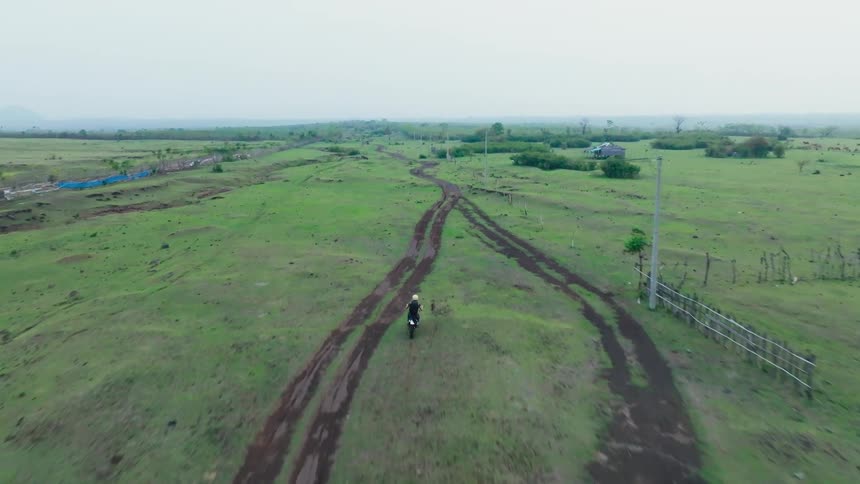 Motorcyclist rides along a dirt road passing through a rural countryside